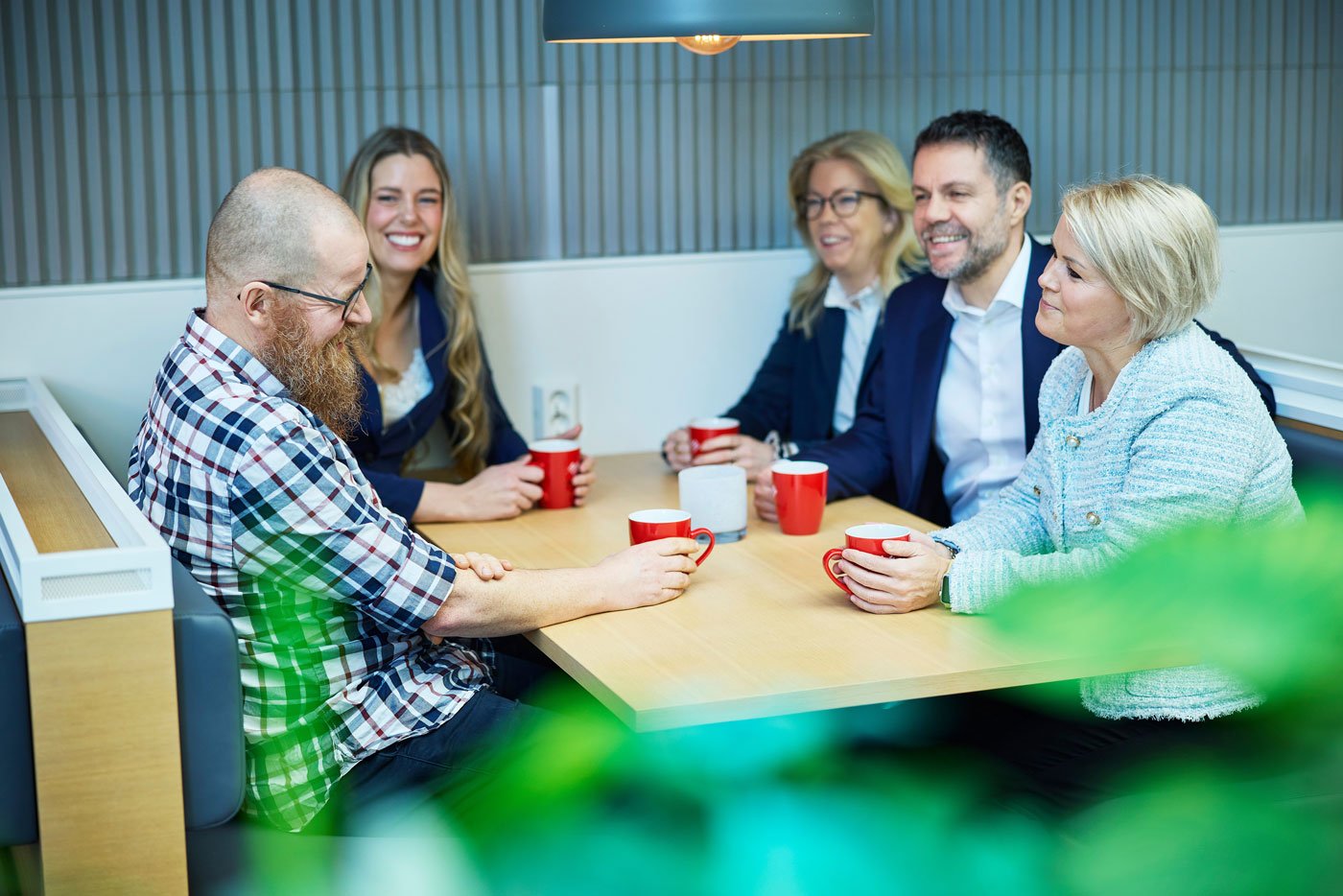 Fem kolleger i samtale rundt et bord med kaffekopper
