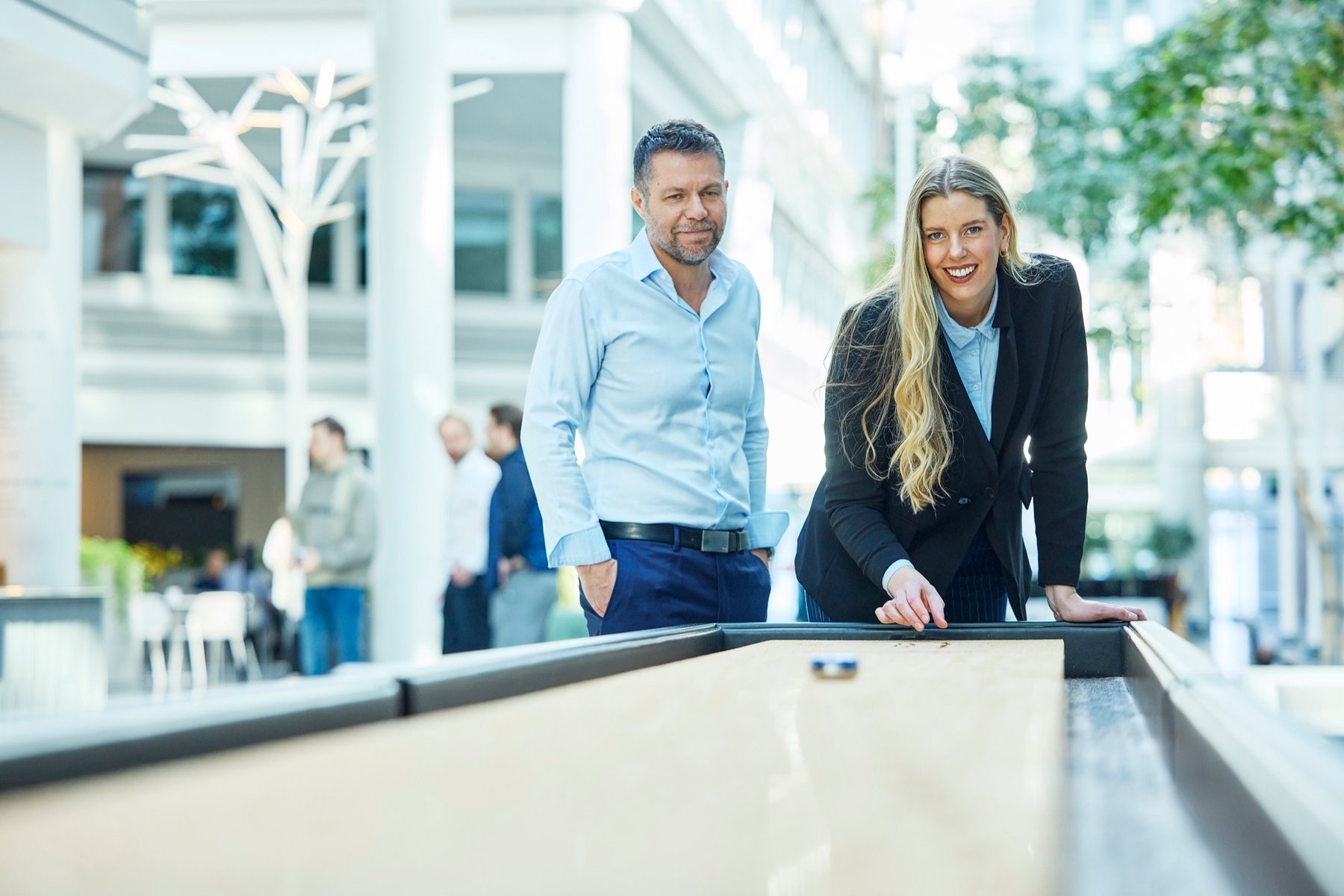 To kolleger ved et shuffleboardbord i et lyst kontorbygg